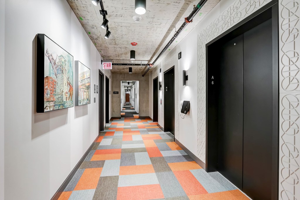 A hallway with a patterned carpet and artwork on the walls.