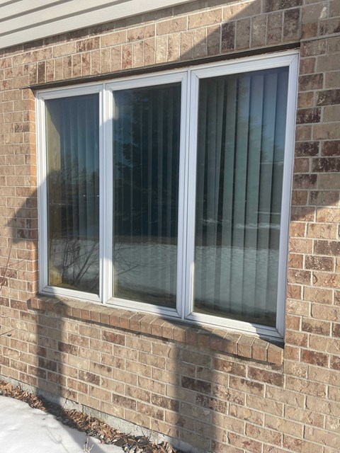A window with white frames and a glass pane is on a brick wall.