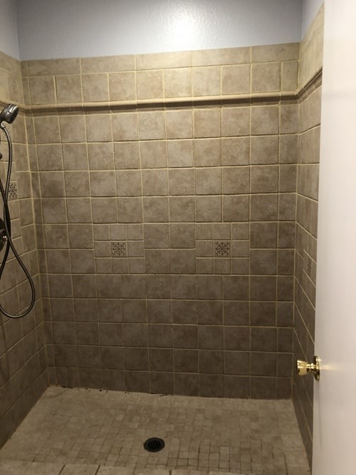 A shower with a tiled wall and floor.