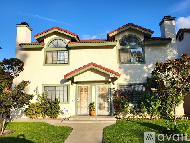 A house with a red roof and a white door is surrounded by greenery.