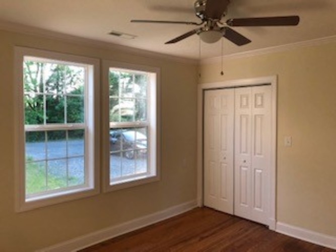 A room with a ceiling fan and two windows.