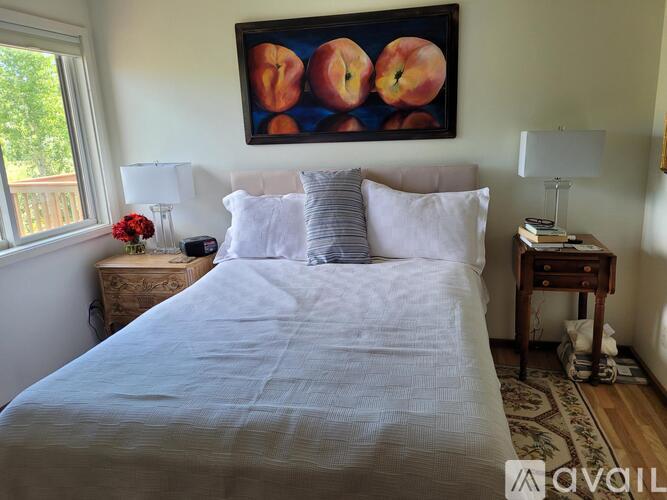 A bedroom with a large bed, a painting of apples above it, and two lamps on either side of the bed.