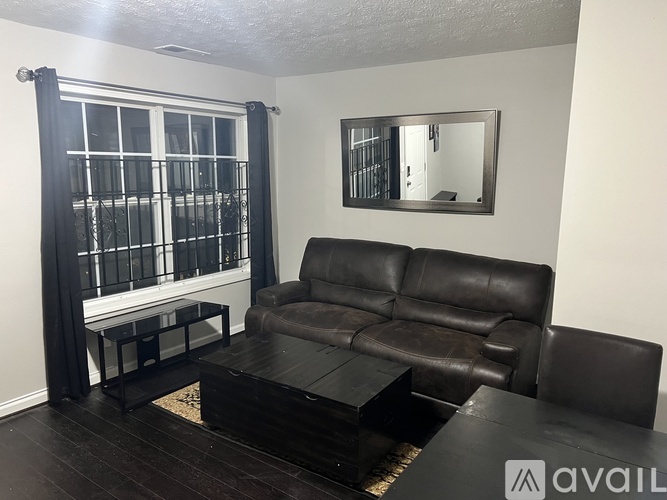 A black leather couch sits in a room with a mirror and a window with black curtains.