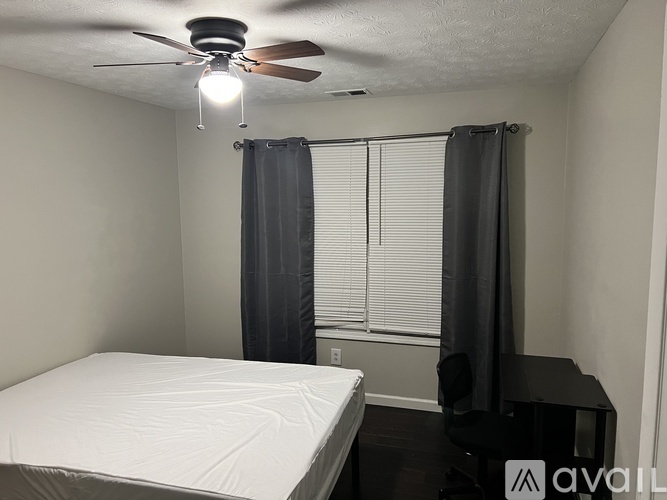 A bedroom with a bed, a ceiling fan, and a window with curtains.