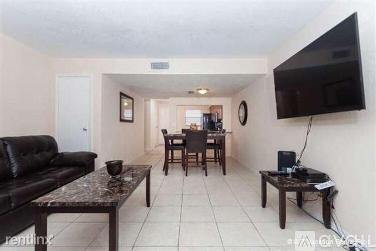 A living room with a black couch, a coffee table, and a flat-screen TV mounted on the wall.