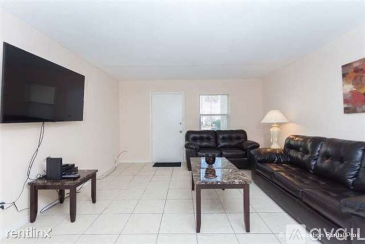A living room with a black leather couch, a wooden coffee table, and a flat-screen TV mounted on the wall.