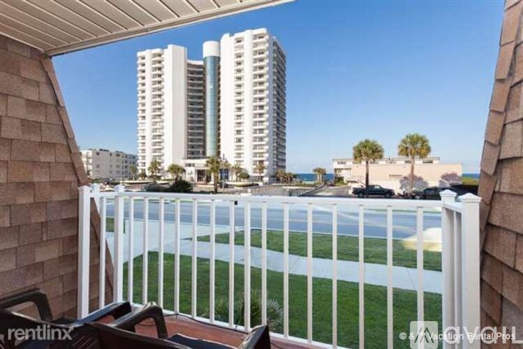 A balcony with a white railing overlooks a beach and buildings.