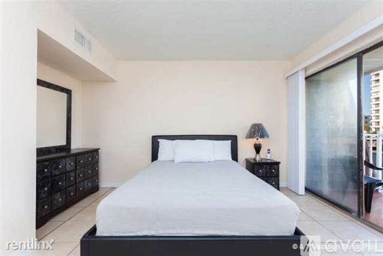 A bedroom with a large bed, a nightstand with a lamp, and a dresser with a mirror.