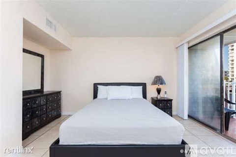 A bedroom with a large bed, a nightstand with a lamp, and a dresser with a mirror.