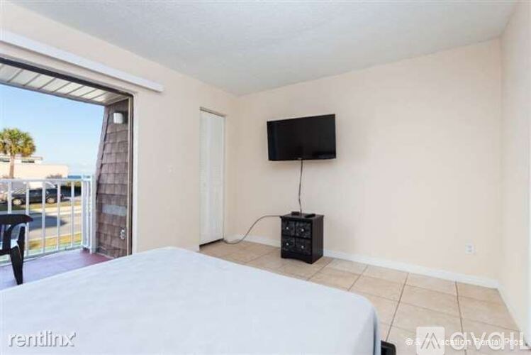 A bed with a white sheet and a logo on it is in a room with a sliding glass door.