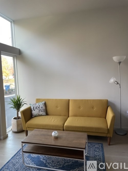 A yellow sofa with a white pillow and a wooden coffee table in front of it.