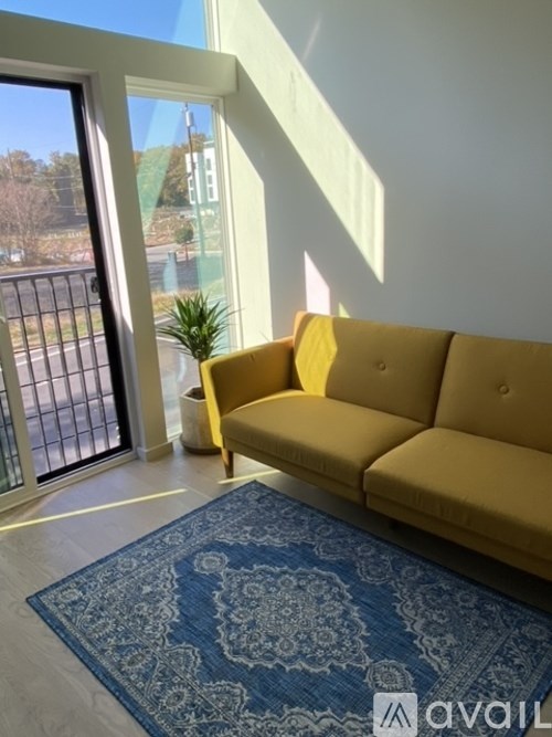 A yellow sofa sits in a room with a blue patterned rug in front of a glass door.