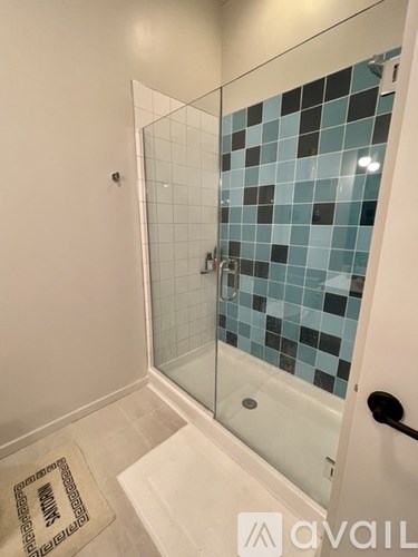 A bathroom with a glass shower door and a black mat on the floor.
