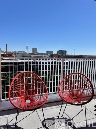 Two red chairs are on a balcony with a city skyline in the background.