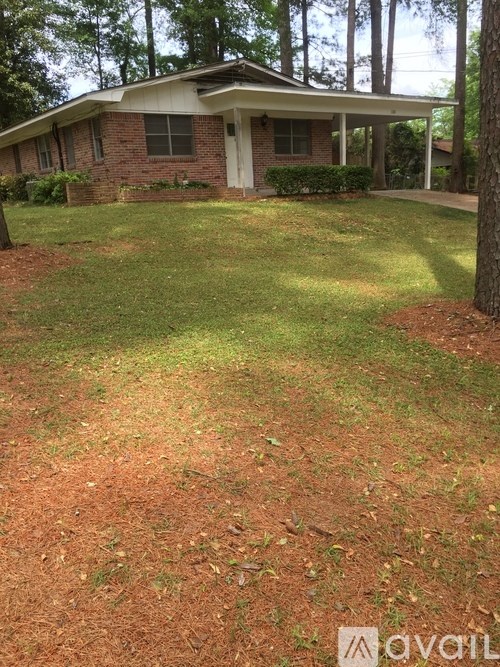 A house with a brown brick exterior and a white door is surrounded by a grassy area with a dirt patch in the foreground.