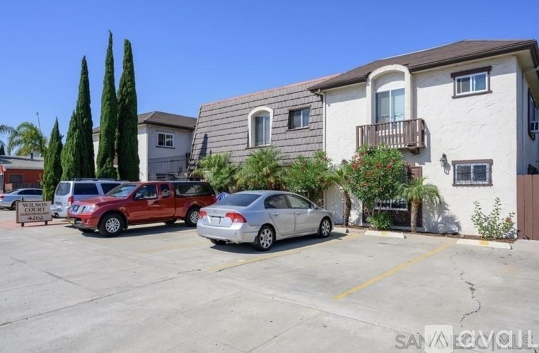 A parking lot with a white car and a red car parked in front of a two-story building.