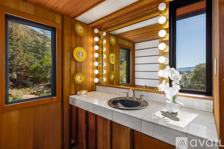 A bathroom with a wooden wall and a large mirror with lights around it.