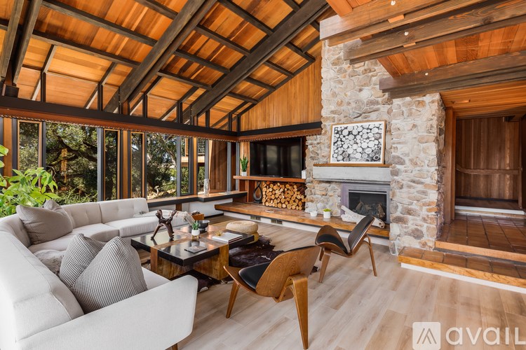 A modern living room with a stone fireplace and wooden beams.