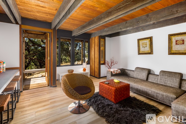 A living room with a brown wicker chair and a red box on a black furry rug.