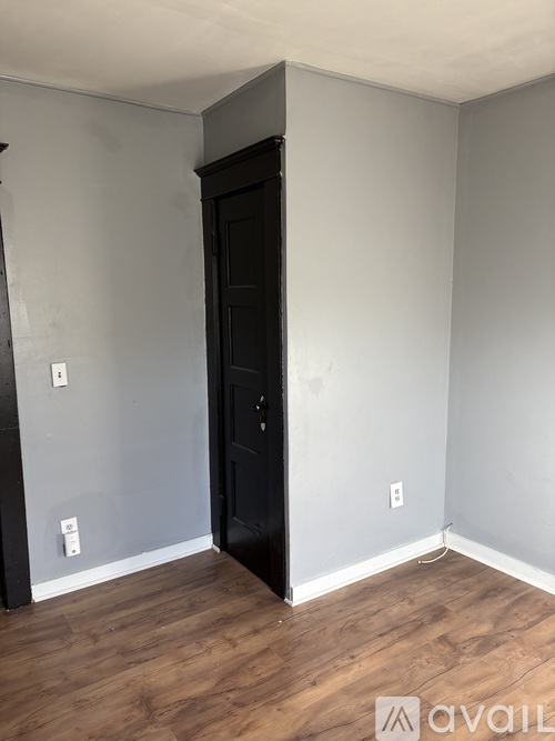 A black door is in a room with wooden floors and white walls.