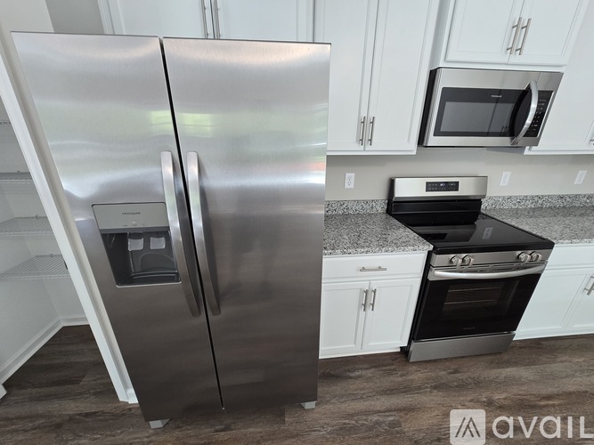 A stainless steel refrigerator stands in a kitchen with a microwave and oven in the background.