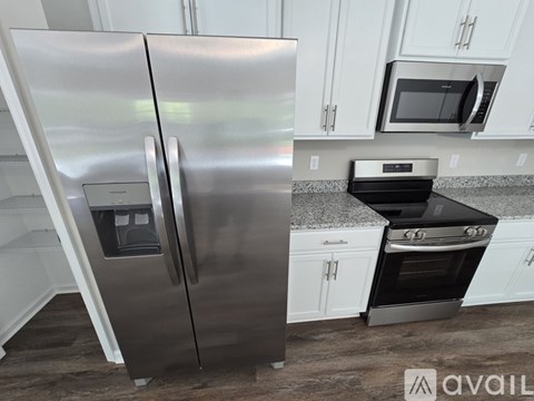 A stainless steel refrigerator stands in a kitchen with a microwave and oven in the background.