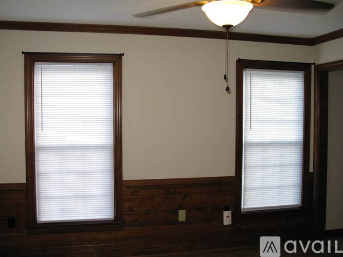 A room with a ceiling fan and two windows with blinds.