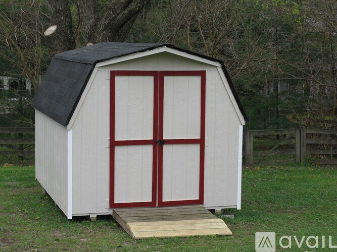 A small white shed with a black roof and red doors.