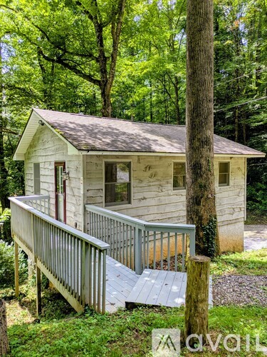 A small white house with a porch is surrounded by trees.