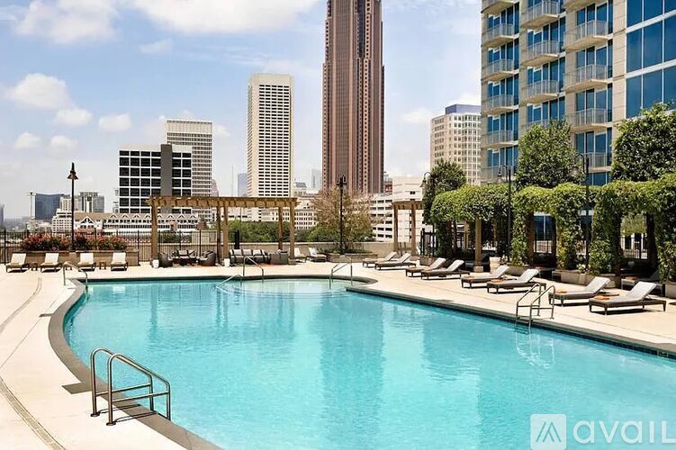 A pool surrounded by lounge chairs and trees with a city skyline in the background.