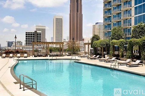 A pool surrounded by lounge chairs and trees with a city skyline in the background.