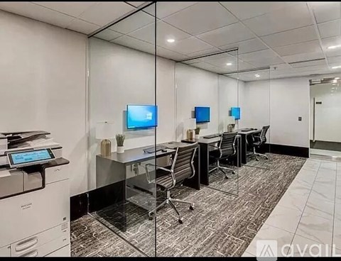 A modern office space with a glass wall, a desk with a computer, and a printer on the left.