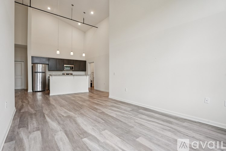A spacious room with wooden flooring and a kitchen area in the background.