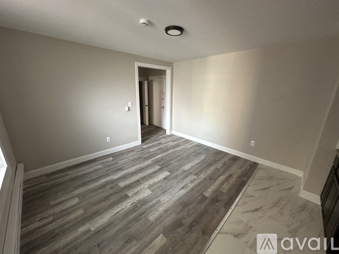 A room with wooden flooring and a doorway leading to another room.