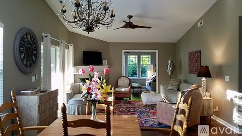 A living room with a wooden table and chairs, a sofa, a television, and a vase of flowers.