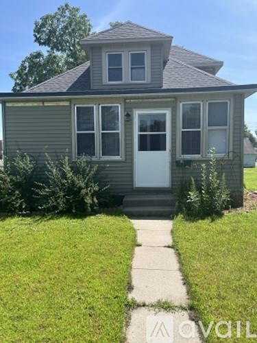 A house with a grey roof and a white door is surrounded by green grass.