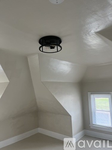 A room with a window and a smoke detector on the ceiling.