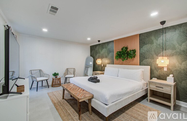 A bedroom with a large bed, a chair, a table, and a wall with a leafy design.