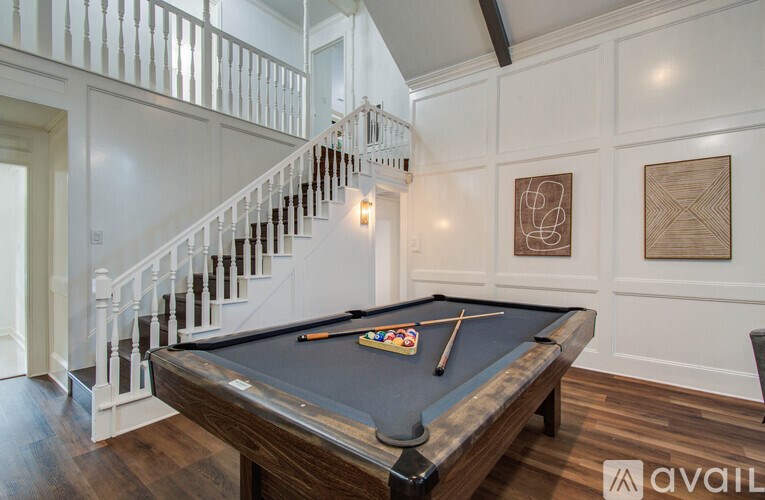A pool table is in the middle of a room with a staircase.