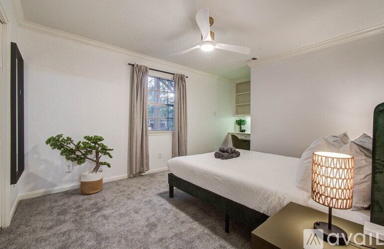 A well-lit bedroom with a bed, a potted plant, and a ceiling fan.