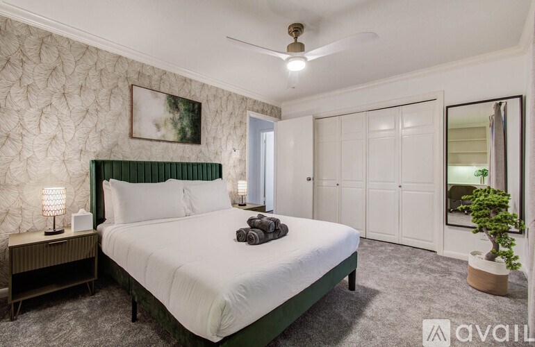 A bedroom with a large bed, a ceiling fan, and a plant.