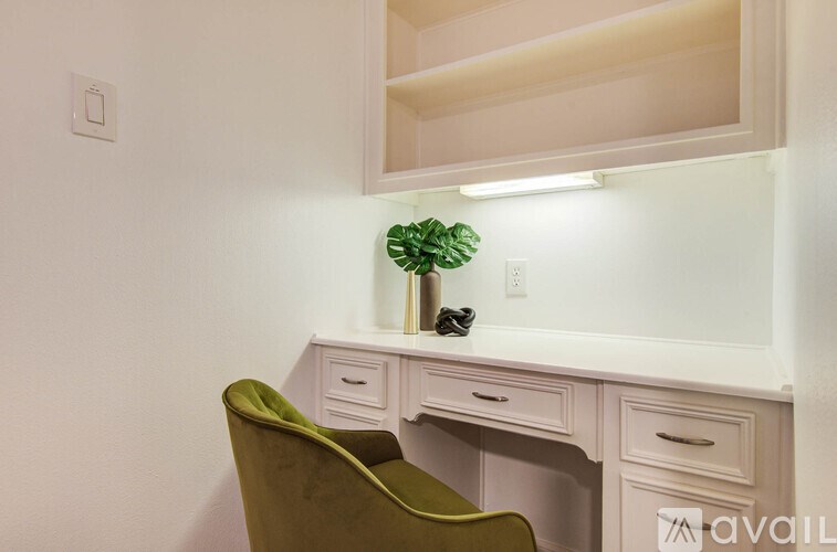 A green chair is in front of a white desk with drawers.