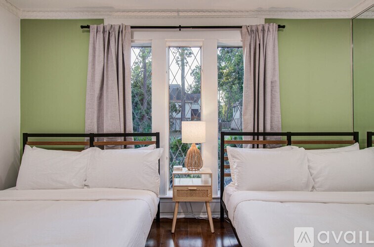 Two beds in a room with green walls and a window with curtains.