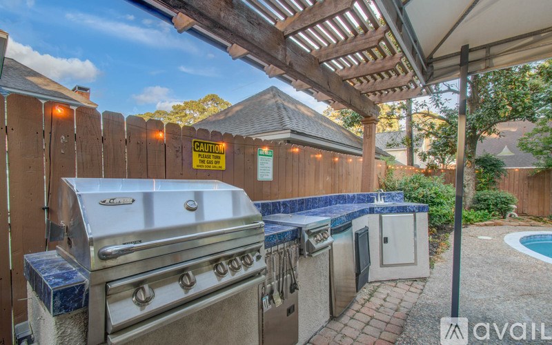 A BBQ grill is in a covered area next to a pool.