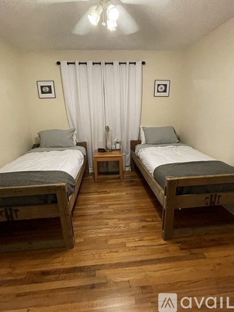 Two beds in a room with wooden floors and white curtains.