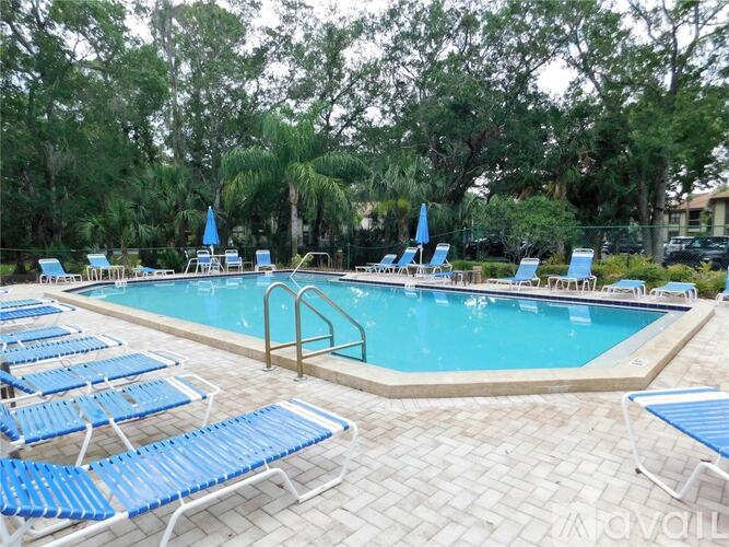A pool surrounded by blue lounge chairs and trees.