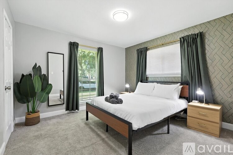 A bedroom with a large bed, a potted plant, and a window with curtains.