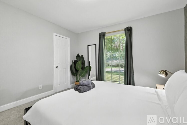 A bedroom with a large bed, a window with green curtains, and a potted plant.