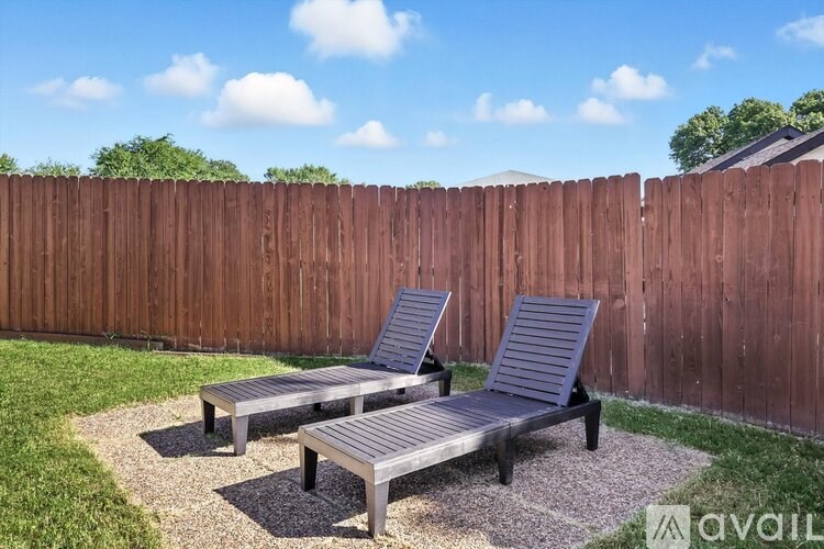 Two grey benches are placed on a gravel area in front of a wooden fence.