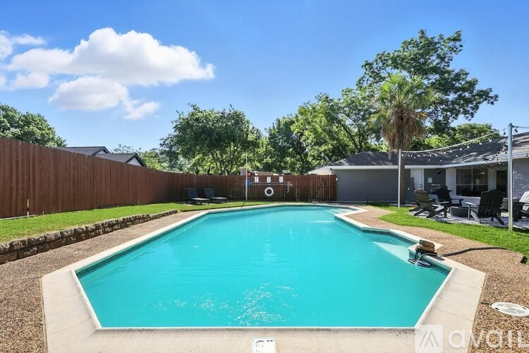 A large swimming pool in a backyard with a wooden fence and trees.